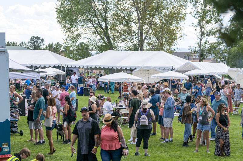 Groups of people mill about on a lawn with white tents and food trucks at Sedona WineFest.